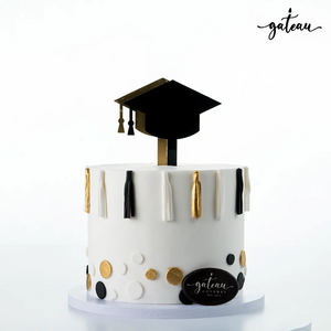 White graduation cake design with black and gold tassels and a black graduation cap topper