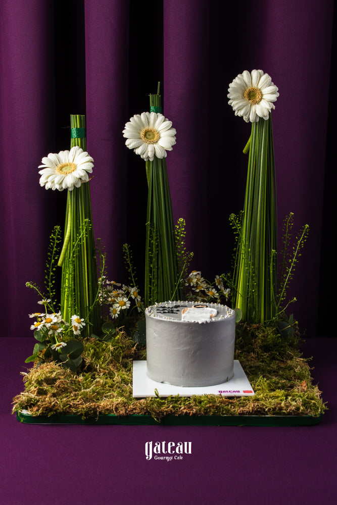 Hajj celebration cake by Gateau Gourmet Cafe displayed with white flowers and green grass on a dark purple background