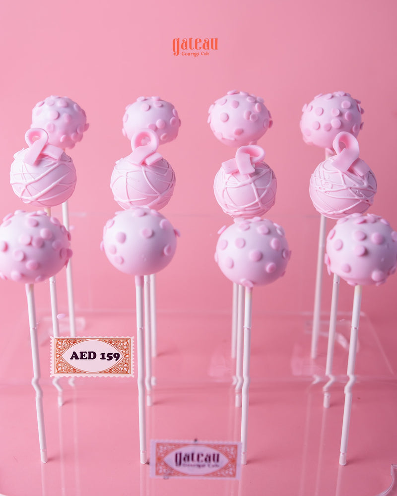Pink handcrafted cake pops from Gateau Gourmet Cafe arranged on white sticks against a pink background