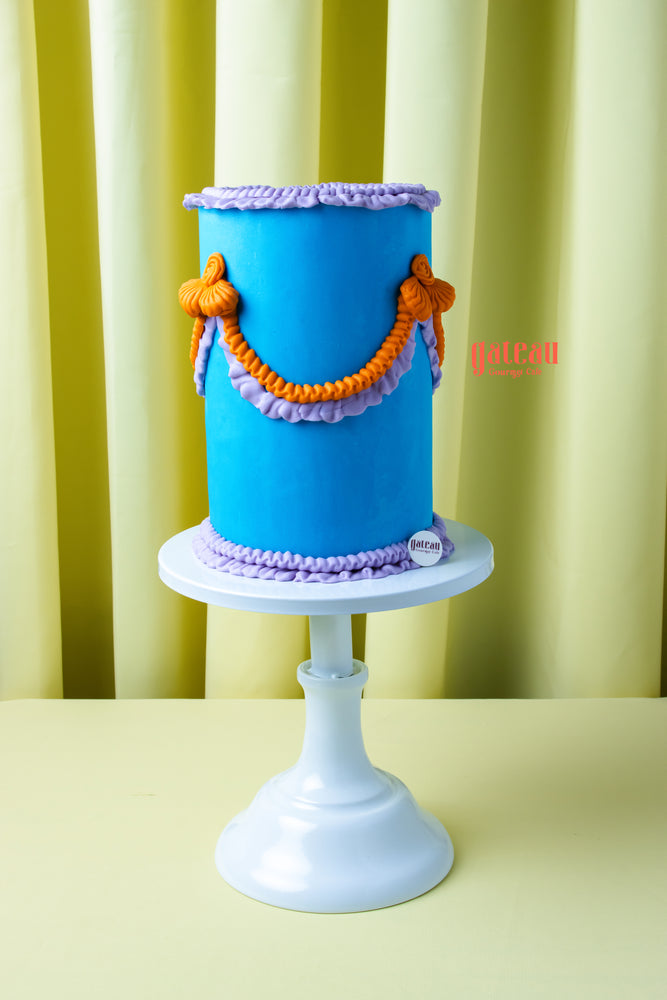 Tall blue handcrafted cake with purple and orange decorative icing from Gateau Gourmet Cafe handcrafted cakes near me