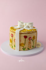Handcrafted gourmet cake decorated with colorful floral icing and a white fondant bow on top