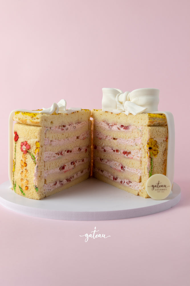 Handcrafted gourmet cake with multiple layers of pink cream and strawberry filling decorated with floral designs and a white bow