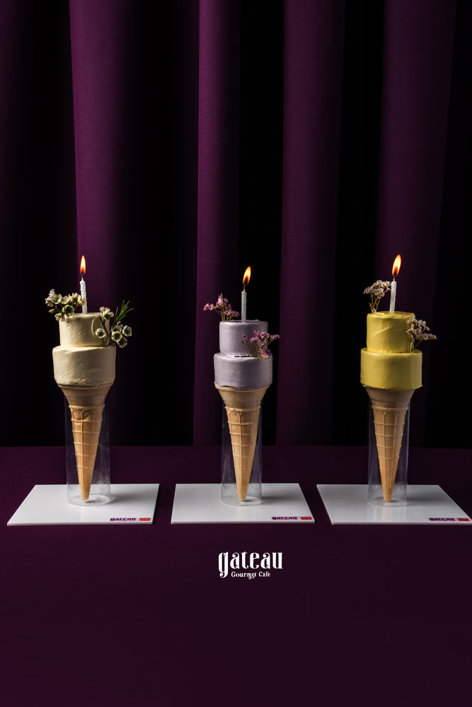 Gateau Gourmet Cafe ice cream cone cake with candles in multiple colors displayed on white plates against a dark purple background