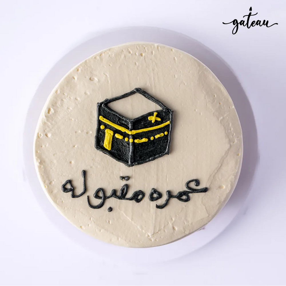 Kaaba themed cake with black and yellow decoration and Arabic script on white frosting