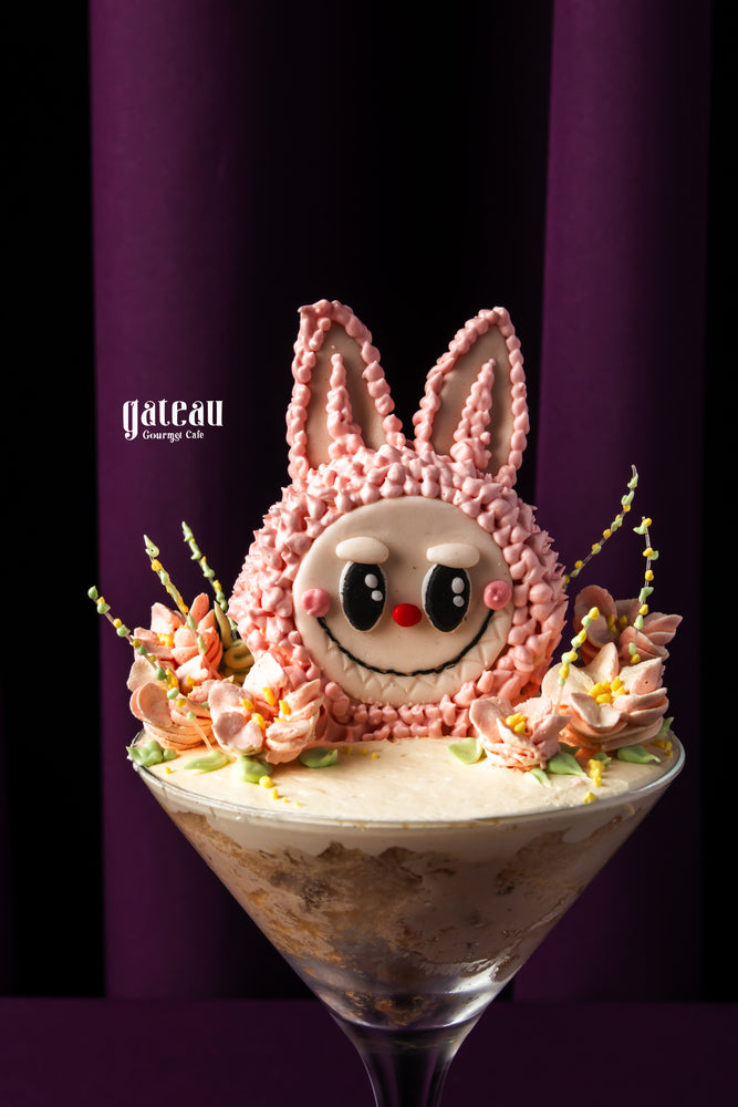Labubu cake topped with pink bunny decoration and fresh flowers, served in a glass dish