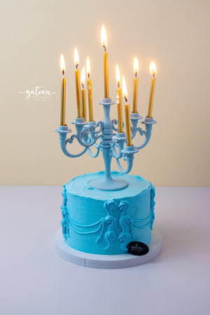 Luxury candelabra cake by Gateau Gourmet Cafe with blue frosting and lit gold candles