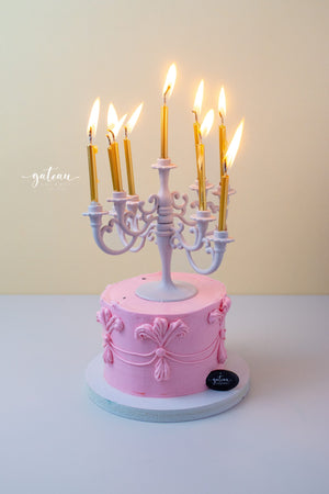 Pink cake from Gateau Gourmet Cafe decorated with a white luxury candelabra cake topper with lit golden candles