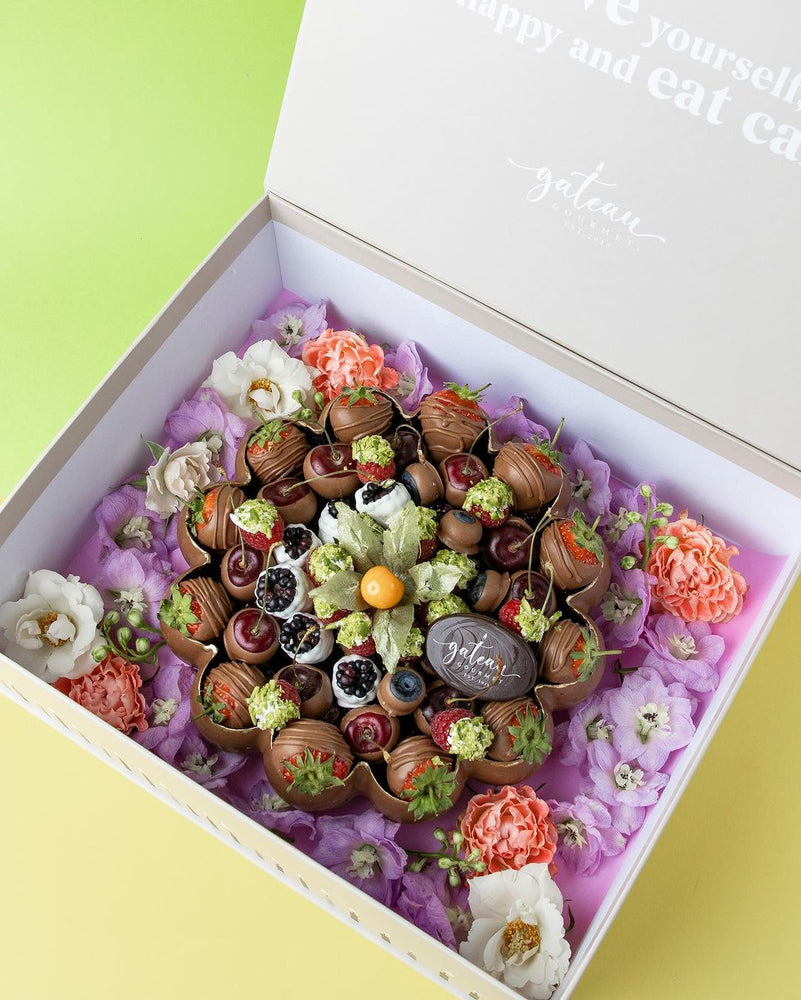 Luxury chocolate dipped fruits arranged in a decorative gift box with fresh flowers by Gateau Gourmet Cafe