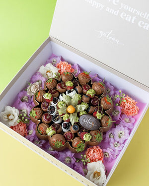 Luxury chocolate dipped fruits arranged in a decorative gift box with fresh flowers by Gateau Gourmet Cafe
