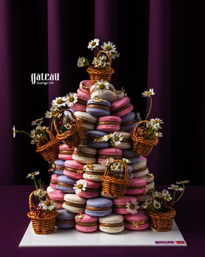 Macaroon tower centerpiece from Gateau Gourmet Cafe decorated with small wicker baskets and white flowers