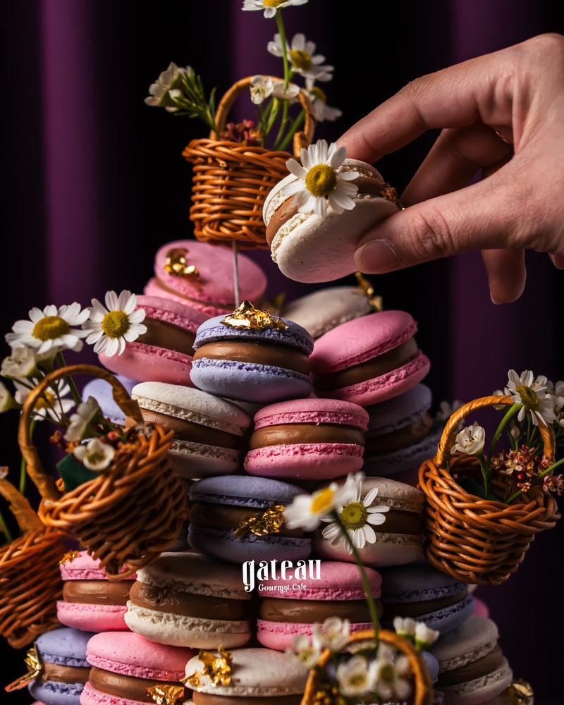 Hand placing a white macaroon decorated with a daisy on a colorful macaroon tower centerpiece with small wicker baskets and flowers