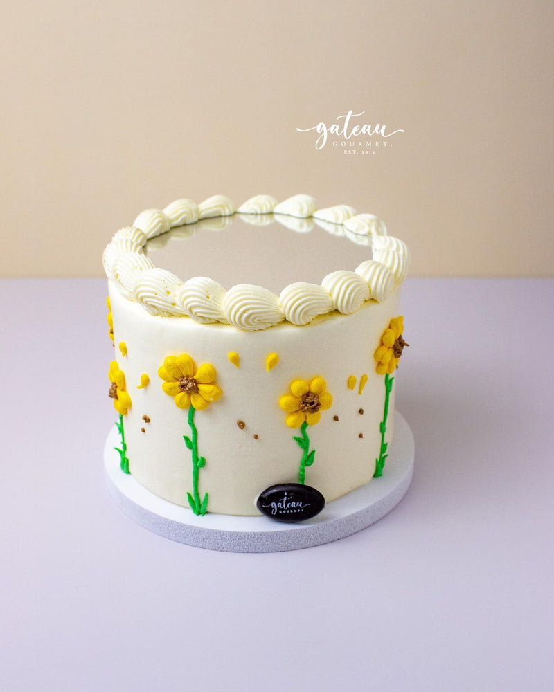 Mirror cake with flowers decorated with yellow floral designs and white piped frosting by Gateau Gourmet Cafe