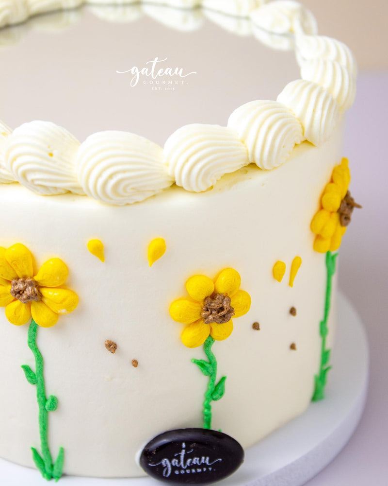 Mirror cake with flowers decorated with yellow floral icing and white whipped cream swirls by Gateau Gourmet Cafe