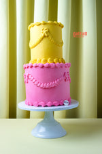Two-tier yellow and pink cake with decorative icing on white stand by Gateau Gourmet Cafe order gourmet cakes online