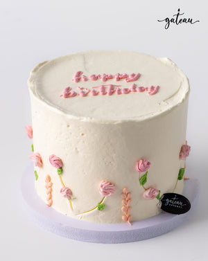 Pastel rose birthday cake with white frosting and pink floral decorations by Gateau Gourmet Cafe