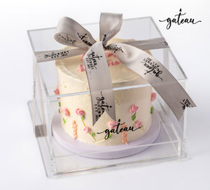 Pastel rose birthday cake with delicate pink icing roses in a clear gift box with a gray ribbon from Gateau Gourmet Cafe