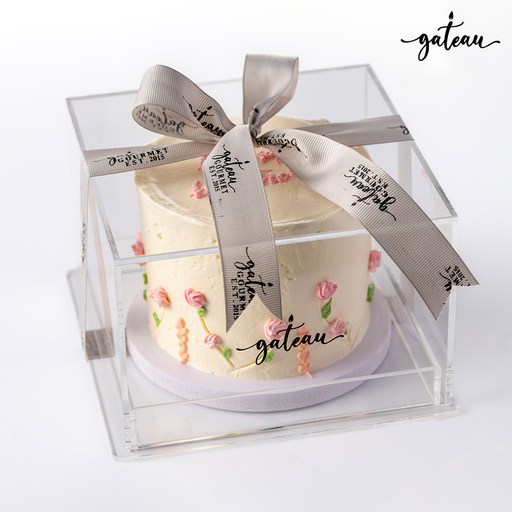 Pastel rose birthday cake with delicate pink rose decorations in a clear box tied with a gray ribbon from Gateau Gourmet Cafe