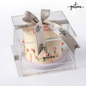 Pastel rose birthday cake with delicate pink rose decorations in a clear box tied with a gray ribbon from Gateau Gourmet Cafe