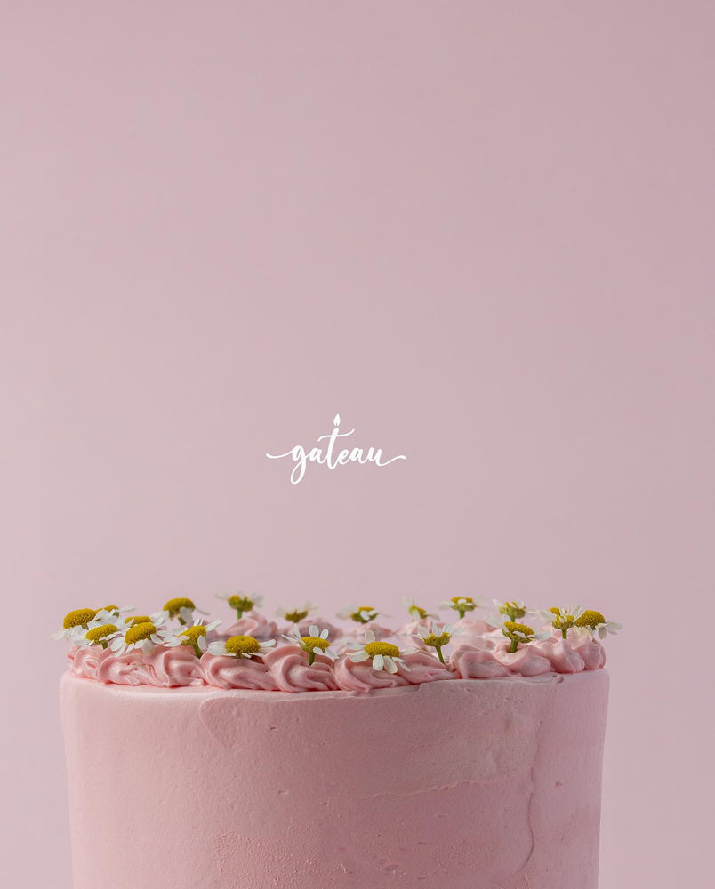 Pink custom mirror cake with delicate pink frosting and small white and yellow flowers on top from Gateau Gourmet Cafe