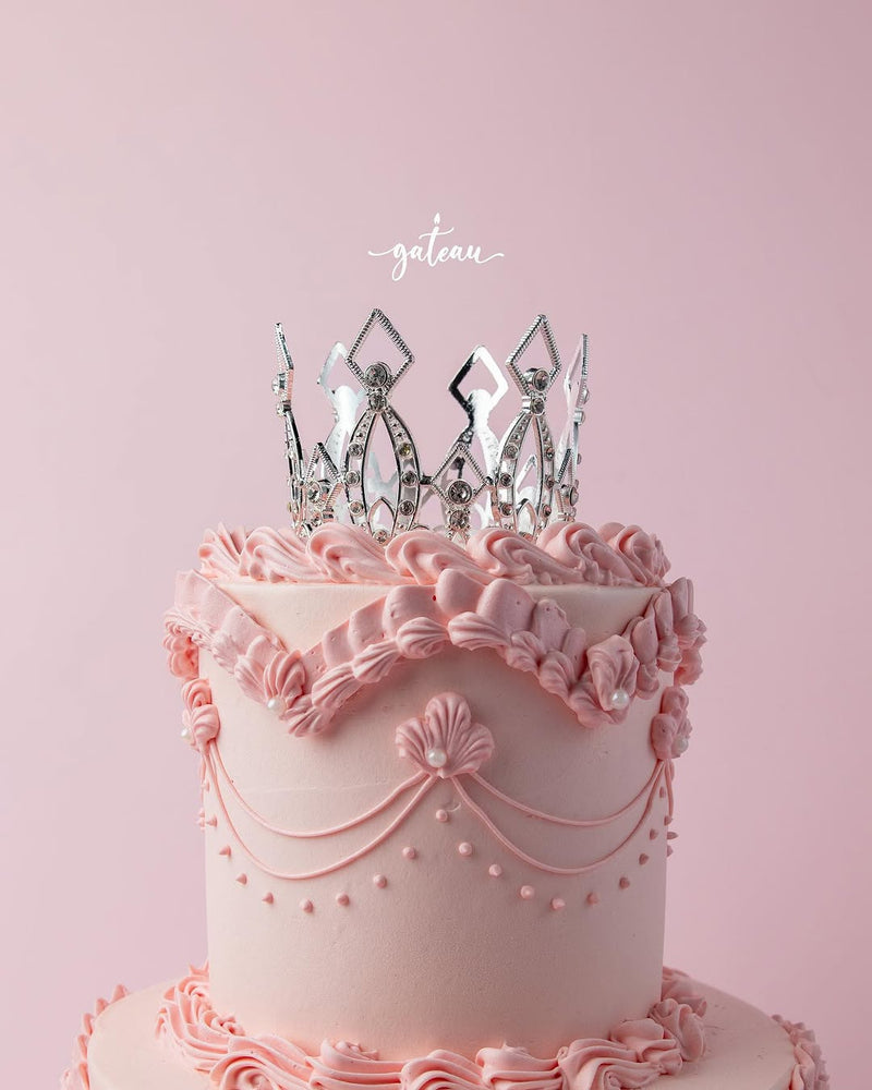Pink royal cake design with intricate icing decorations and a silver crown topper by Gateau Gourmet Cafe
