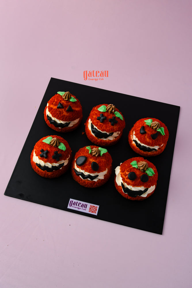 Six pumpkin choux pastry decorated with smiling faces and green leaves on a black platter