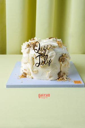 Queen of July birthday cake from Gateau Gourmet Cafe with white frosting and decorative gold accents