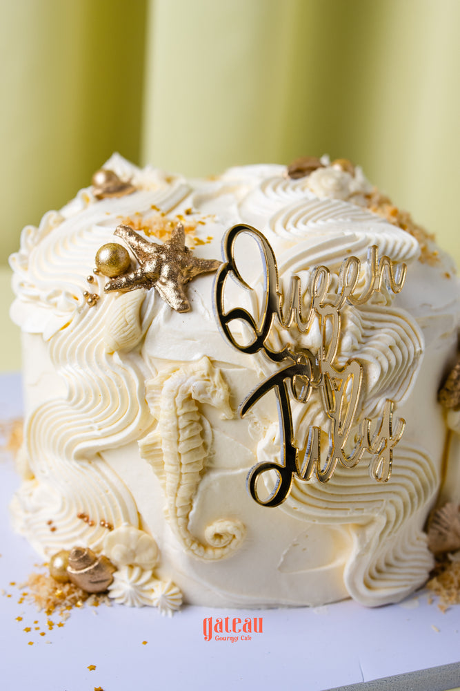 Queen of July birthday cake from Gateau Gourmet Cafe decorated with white frosting and gold ocean-themed accents