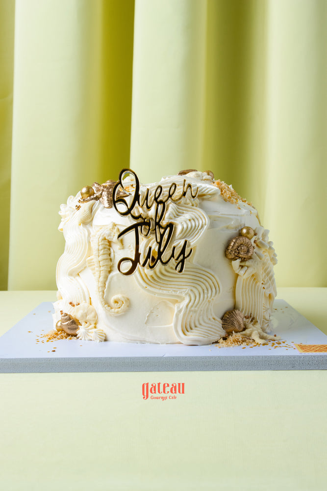 Queen of July birthday cake by Gateau Gourmet Cafe with white frosting and decorative seashells