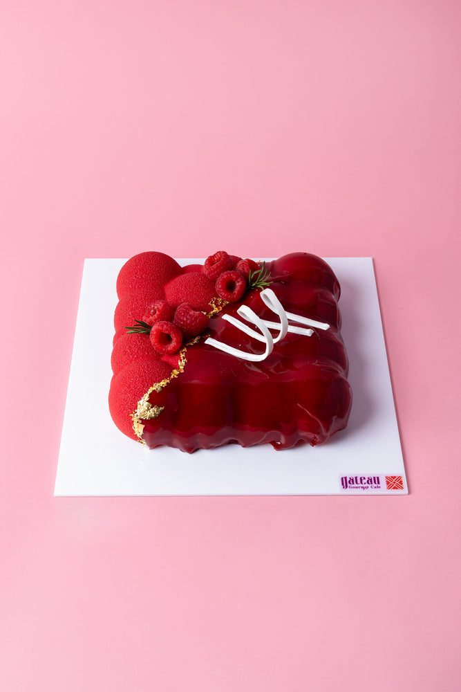 Raspberry Vanilla Mousse Cake from Gateau Gourmet Cafe adorned with fresh raspberries and decorative white accents