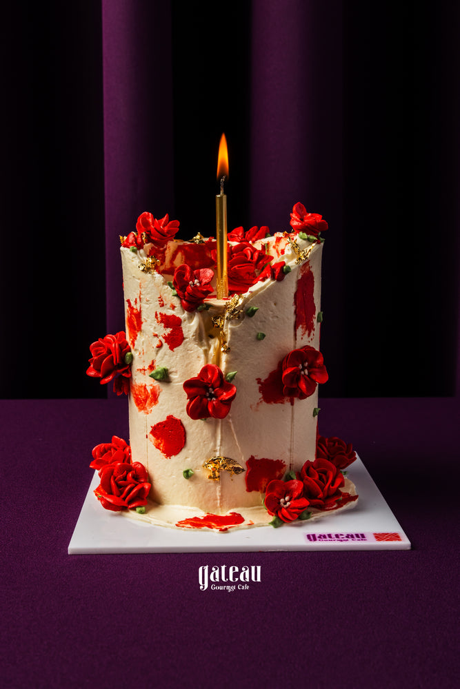 Red floral garden cake by Gateau Gourmet Cafe decorated with red flowers and a lit gold candle