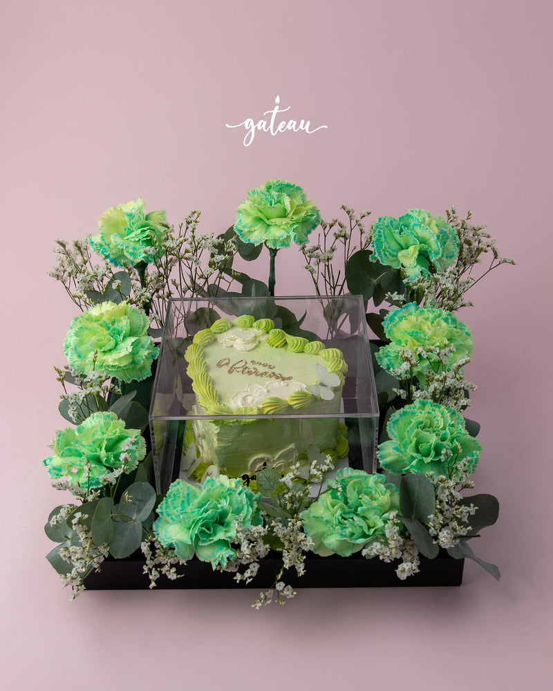 Romantic floral cake arrangement by Gateau Gourmet Cafe featuring a heart-shaped cake surrounded by green flowers and delicate white accents