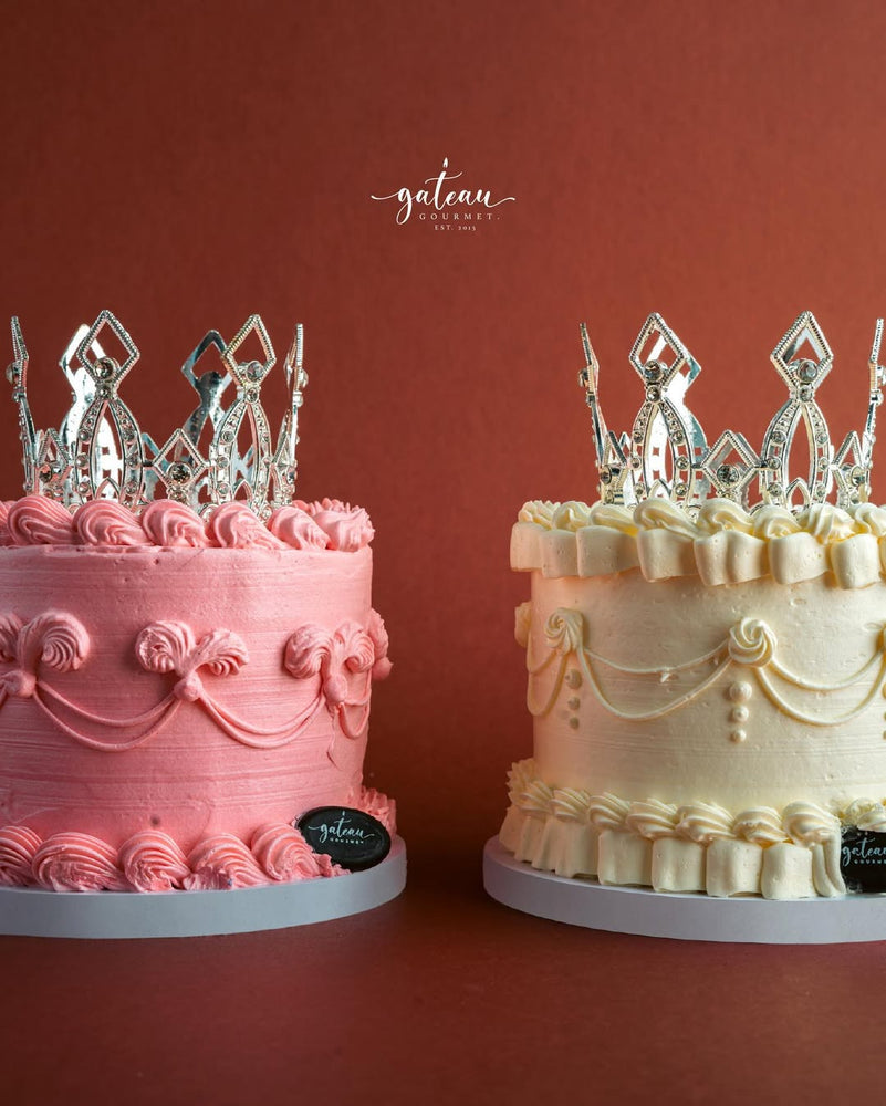 Gateau Gourmet Cafe royal crown cake in pink and white with intricate frosting and silver crown toppers
