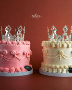 Gateau Gourmet Cafe royal crown cake in pink and white with intricate frosting and silver crown toppers