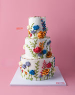 Three-tier cake with colorful spring flowers cake design by Gateau Gourmet Cafe on pink background