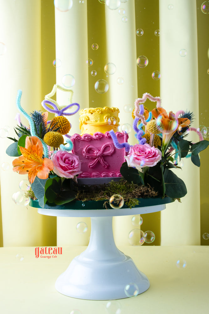 Gateau Gourmet Cafe summer buttercream flower cake with pink and yellow layers decorated with flowers on white cake stand