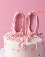 Tailored birthday cake for her featuring pink ballet slippers and decorative ribbons on a cream base