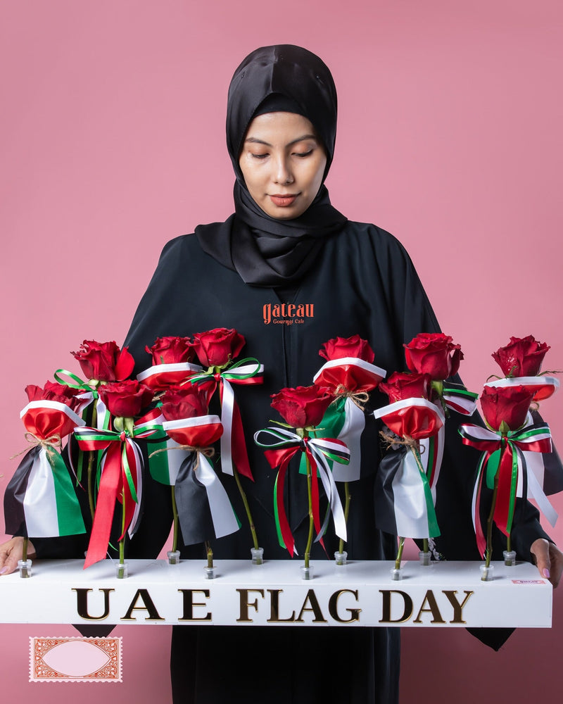 A woman wearing a black hijab holds a display of UAE Flag Day roses arranged with ribbons in national colors