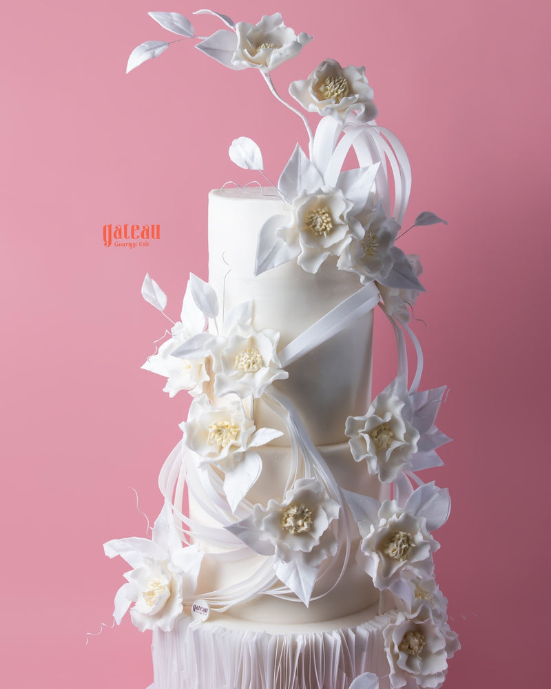 Elegant white tiered wedding cake with delicate floral decorations showcasing unique wedding cake designs by Gateau Gourmet Cafe