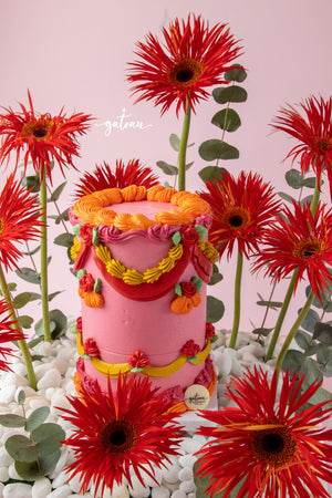 Vibrant floral cake arrangement by Gateau Gourmet Cafe featuring a pink cake decorated with colorful icing surrounded by red flowers