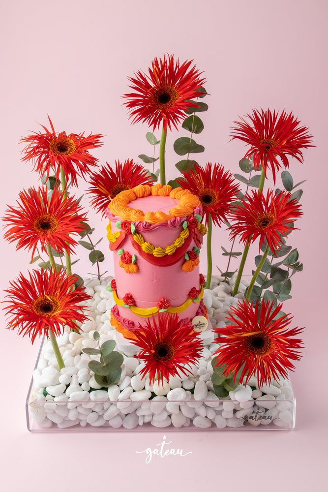 Vibrant floral cake arrangement with bright red flowers and pink decorative cake by Gateau Gourmet Cafe