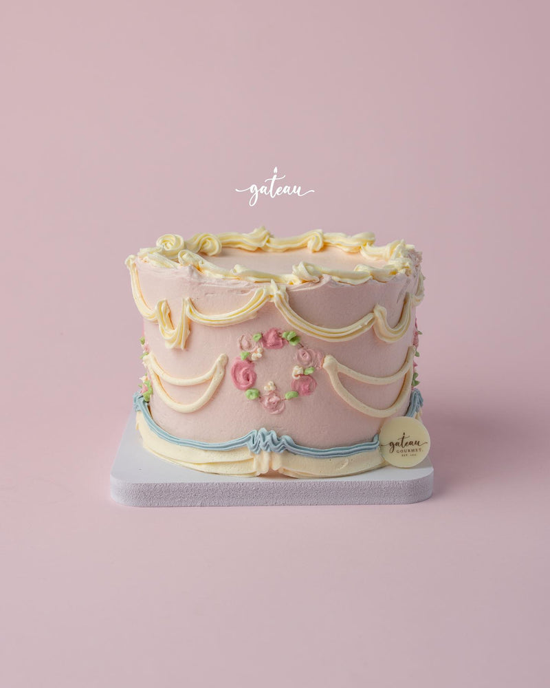 Vintage Buttercream Drape Cake with colorful floral decorations and elegant draping on a light pink background.