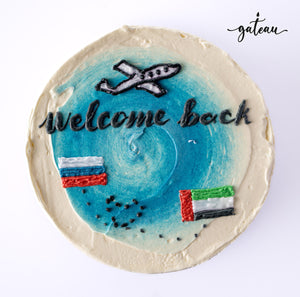 Gateau Gourmet Cafe welcome back cake decorated with an airplane and flags on a blue background