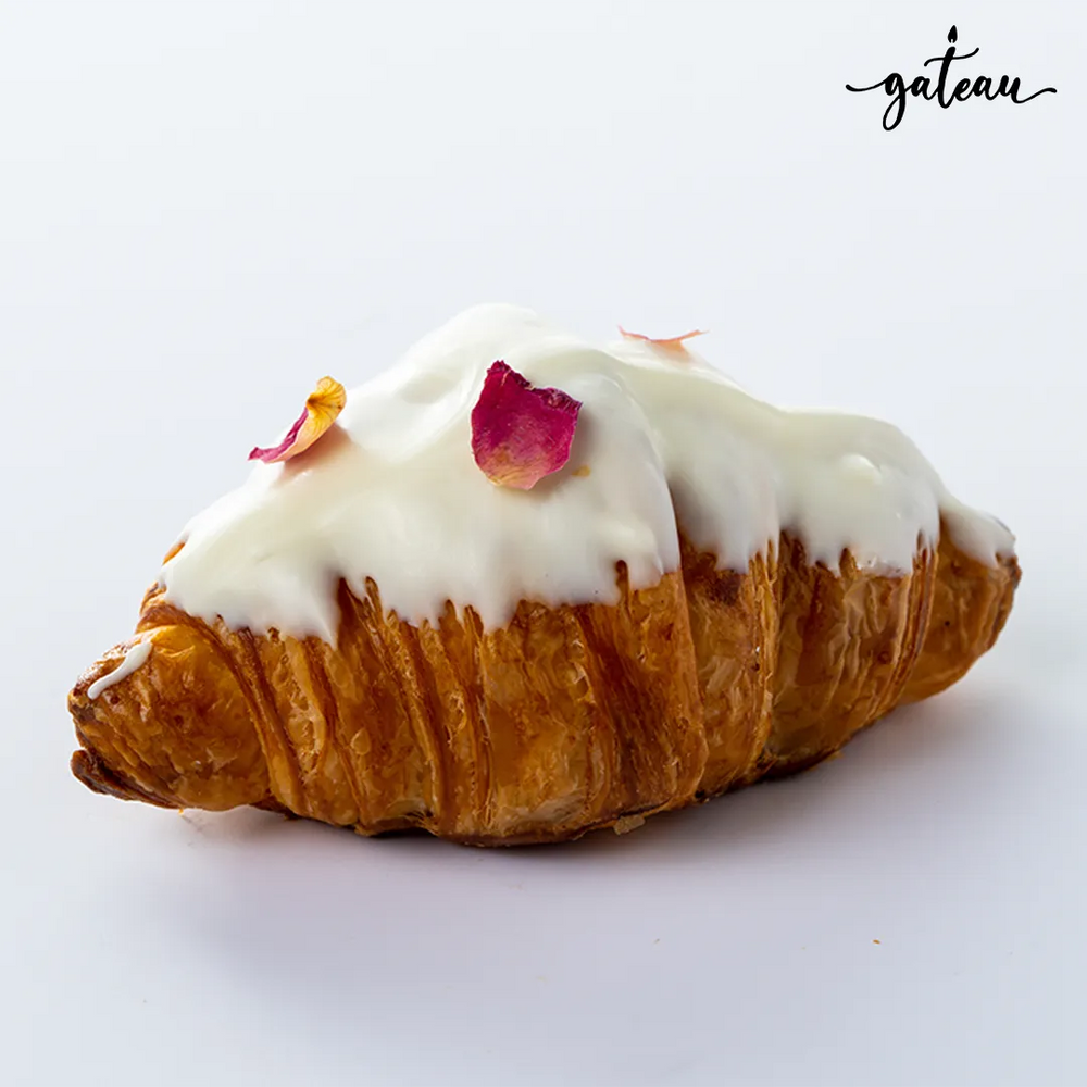 Gateau Gourmet Cafe white chocolate croissant topped with white icing and rose petals on a white background