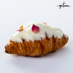 Gateau Gourmet Cafe white chocolate croissant topped with white icing and rose petals on a white background