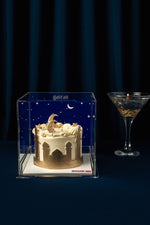 Gilded twilight mini cake in a clear display case with gold accents and decorative frosting