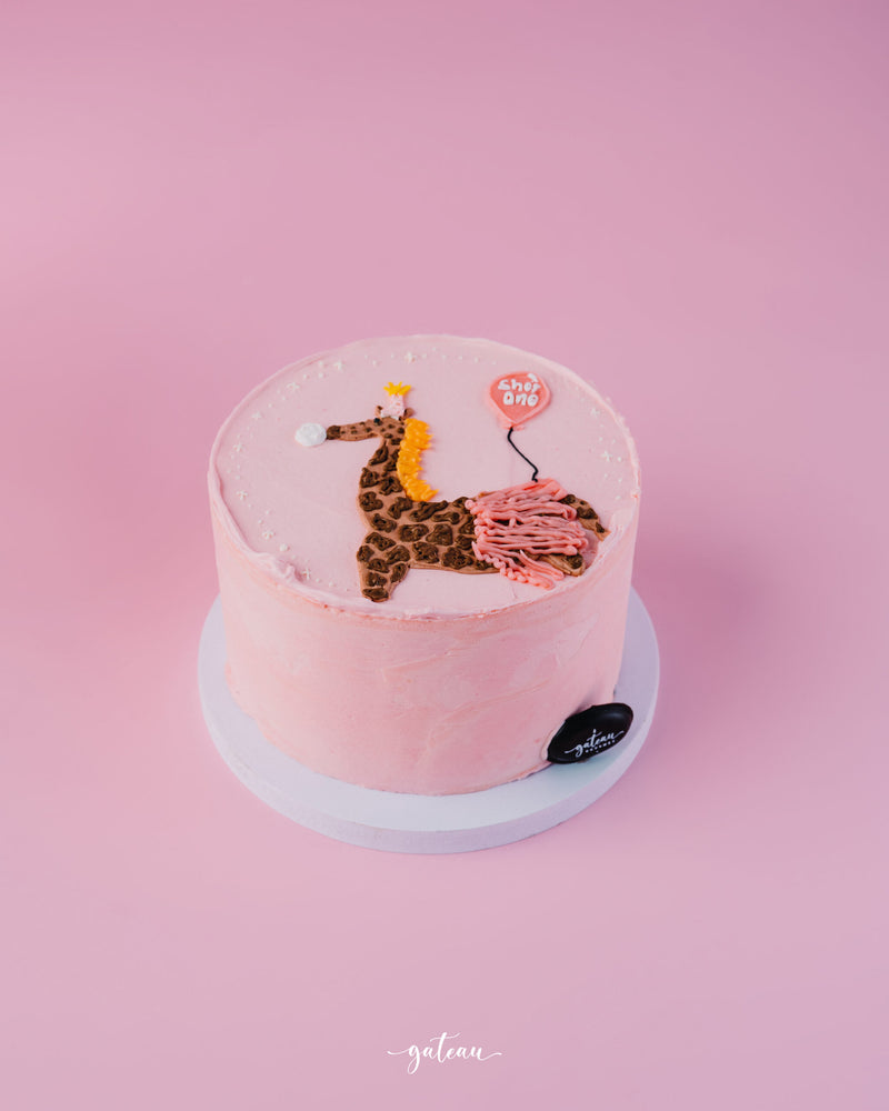 Pink birthday cake with giraffe cake design for birthday featuring balloon and crown decoration