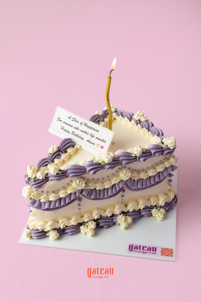 Purple and white gourmet birthday cake slice with candle and decorative flowers from Gateau Gourmet Cafe, gourmet birthday cakes near me
