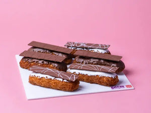 Gateau Gourmet Cafe gourmet chocolate eclairs with glossy chocolate glaze and decorative chocolate strips on white tray