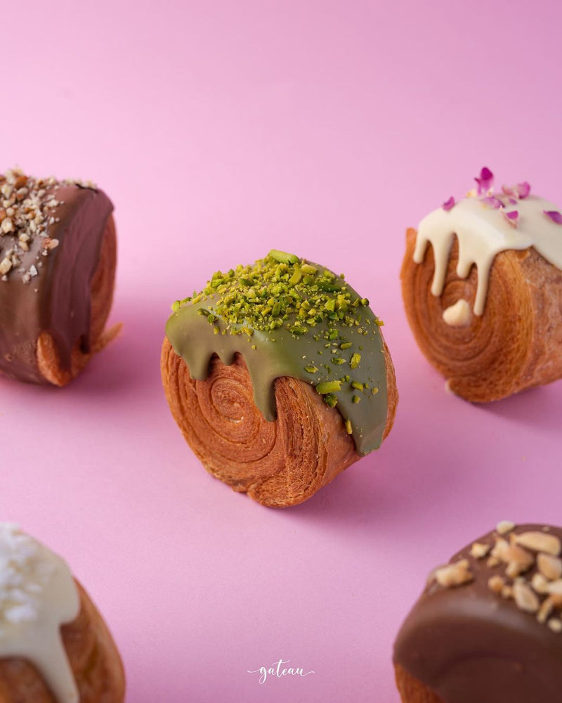 Gateau Gourmet Cafe gourmet croissant rolls with various chocolate and nut toppings on pink background