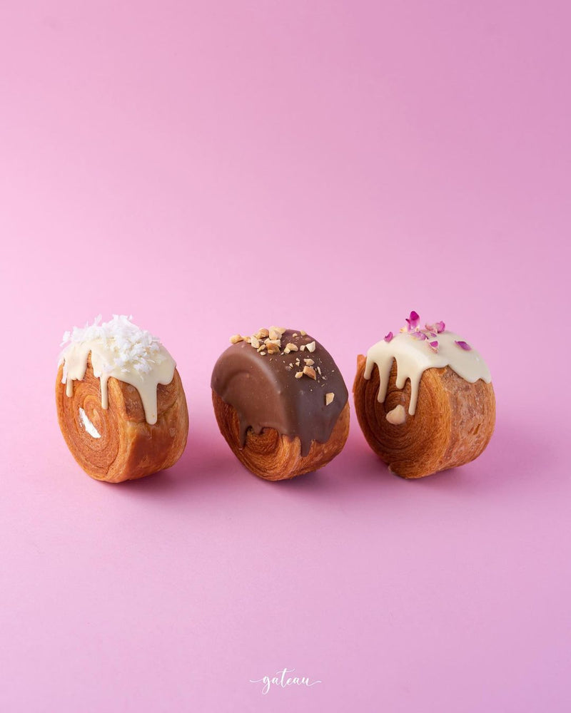 Gateau Gourmet Cafe gourmet croissant rolls with white, chocolate, and vanilla icing on pink background